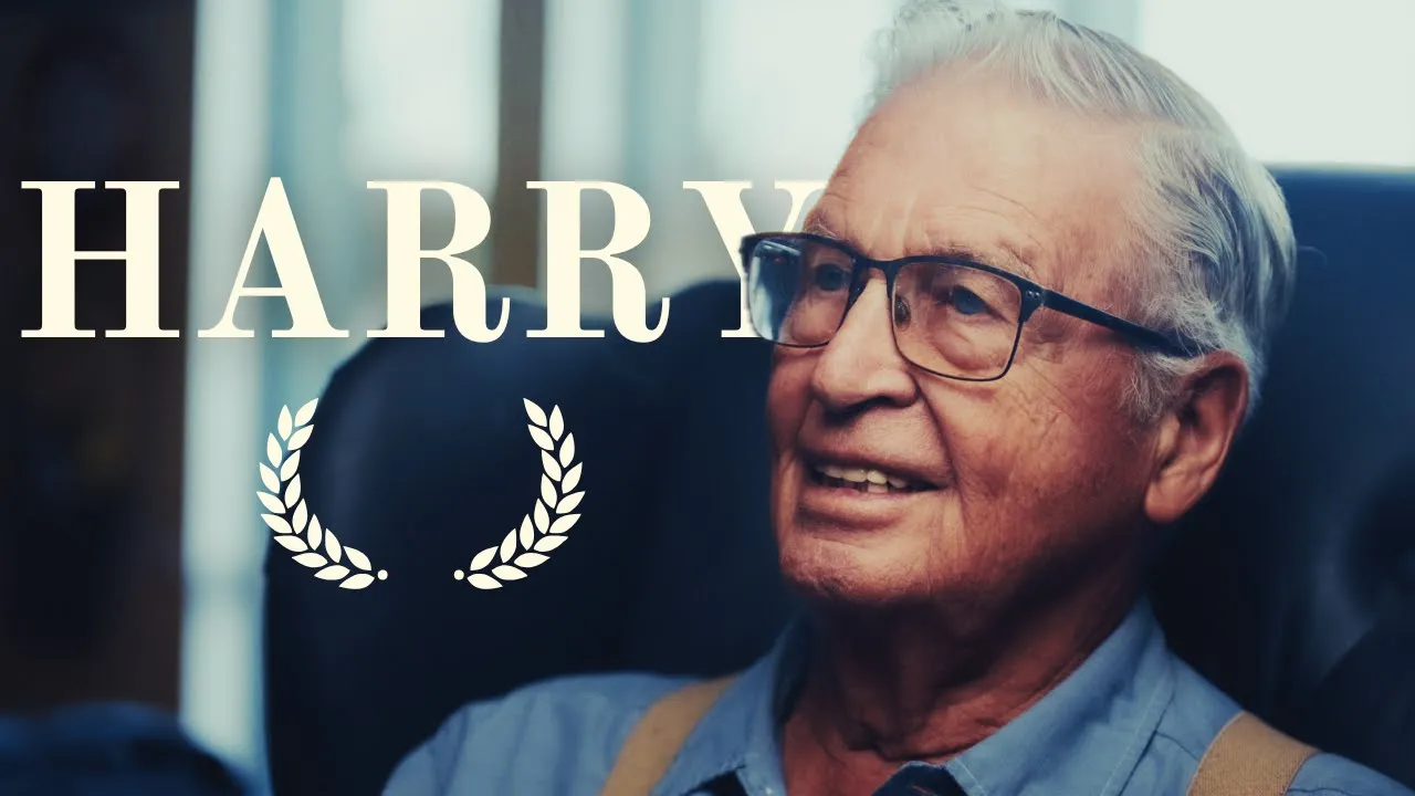 Harry, an older man in glasses and suspenders, smiling as he tells a story at home.